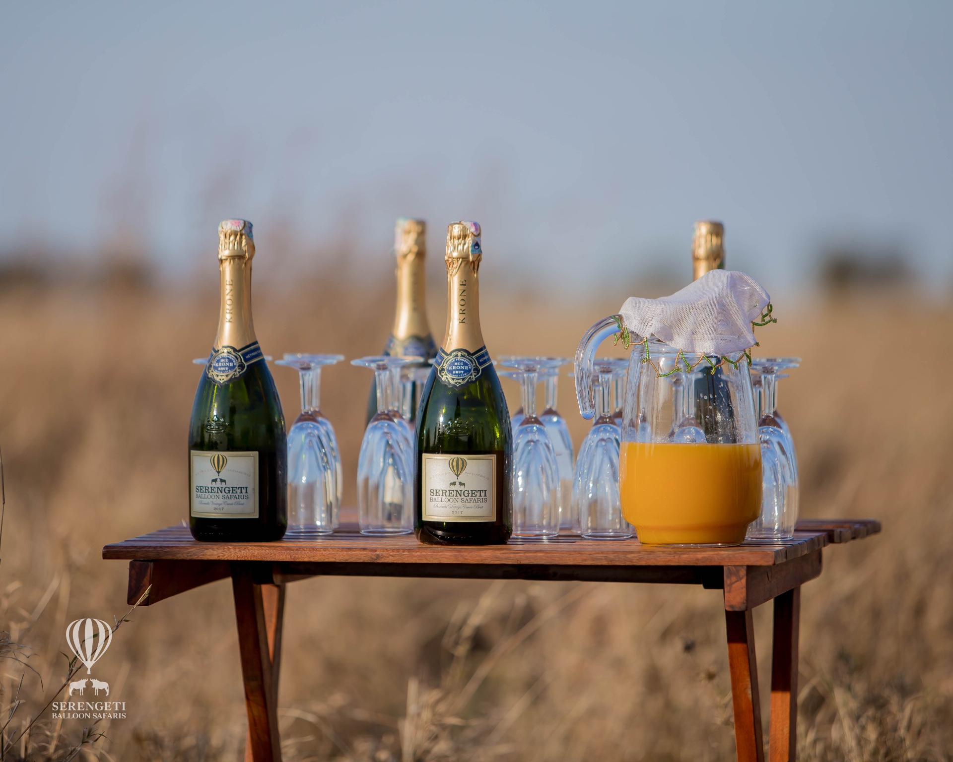 Champagne and glasses set on a wooden table in the bush at golden hour